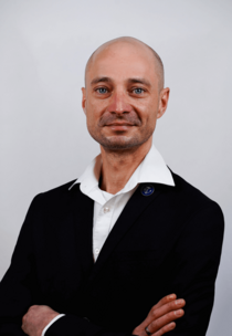 Porträtfoto eines Mannes mit Halbglatze, hellem Hemd und dunklem Sakko.